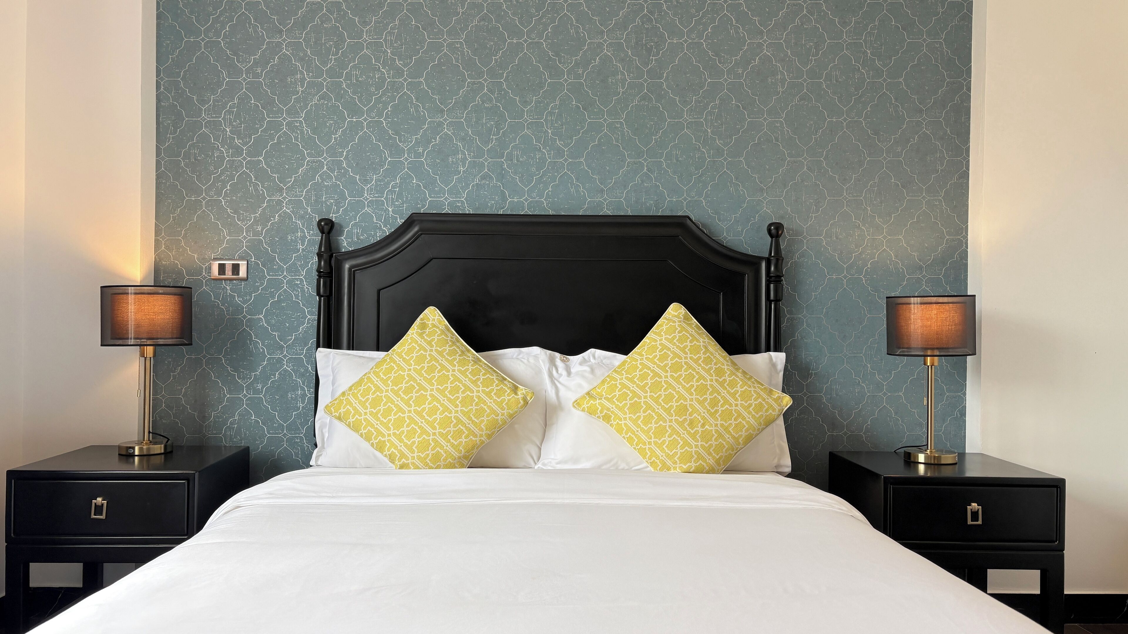 A bed with white bedding and two yellow patterned pillows, flanked by black nightstands with lamps.