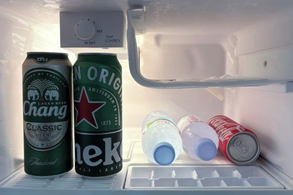 Un refrigerador con dos latas de cerveza Chang y una lata de Heineken, junto con varias botellas.