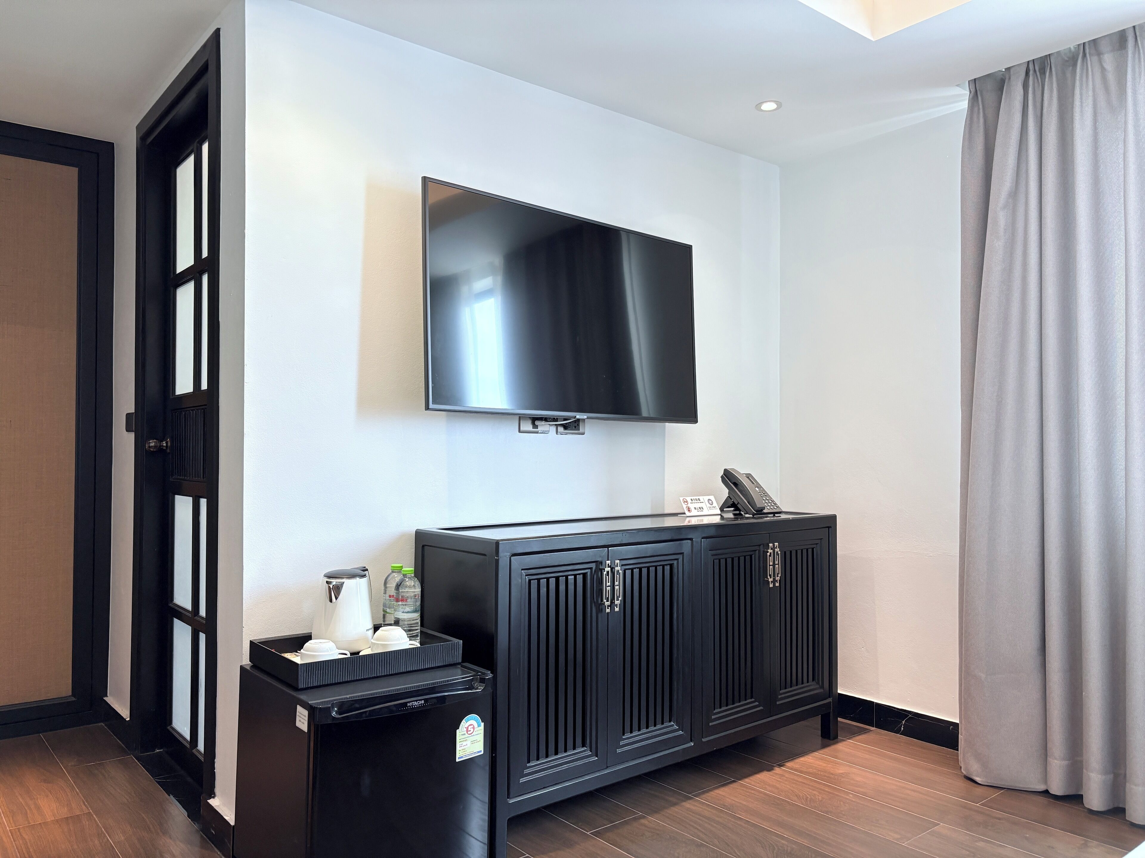 Une chambre d’hôtel moderne dotée d’un téléviseur à écran plat fixé au mur, d’un minibar et d’un meuble en bois foncé.