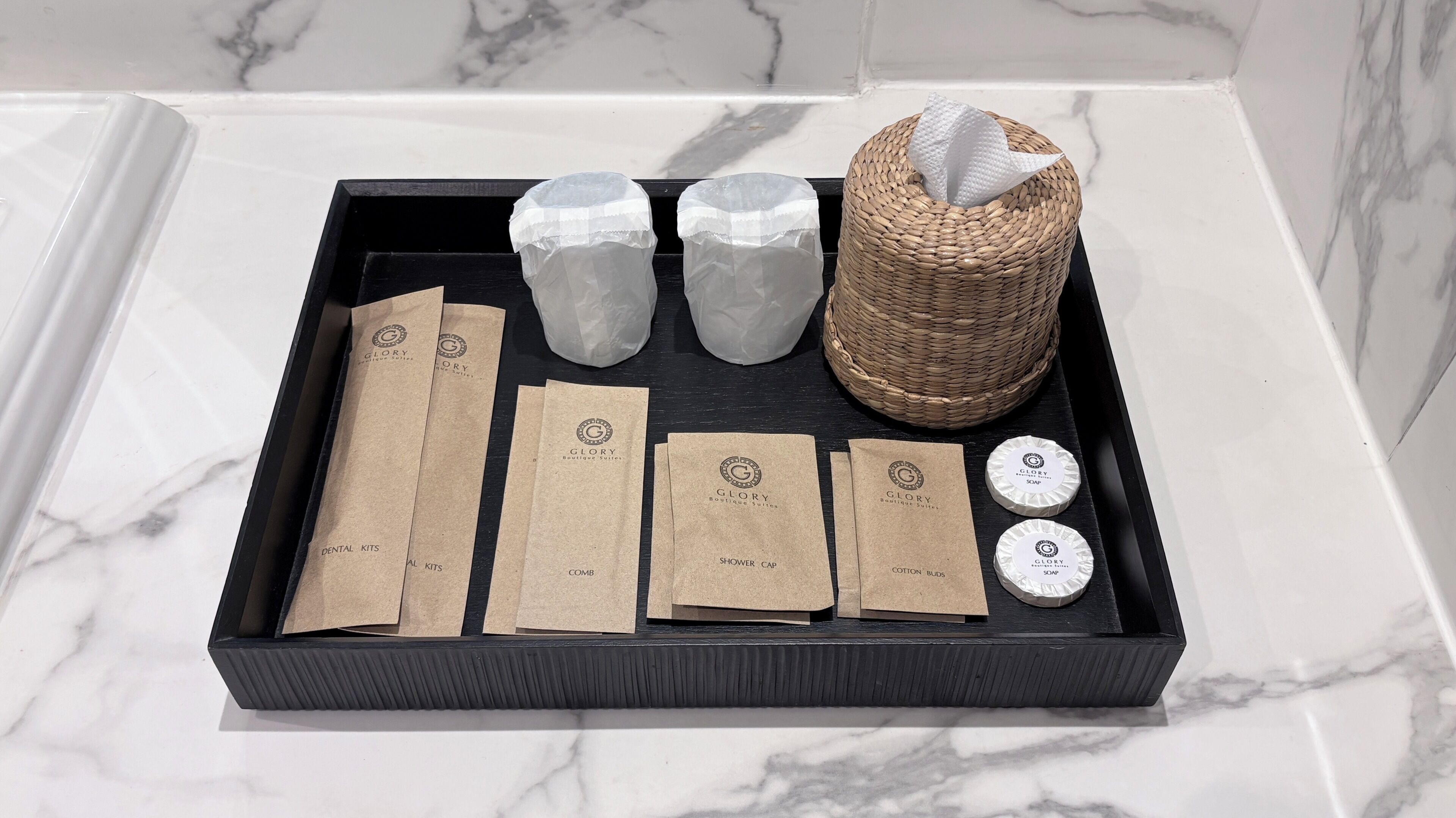 A black tray with various toiletries and a woven basket on a marble surface.