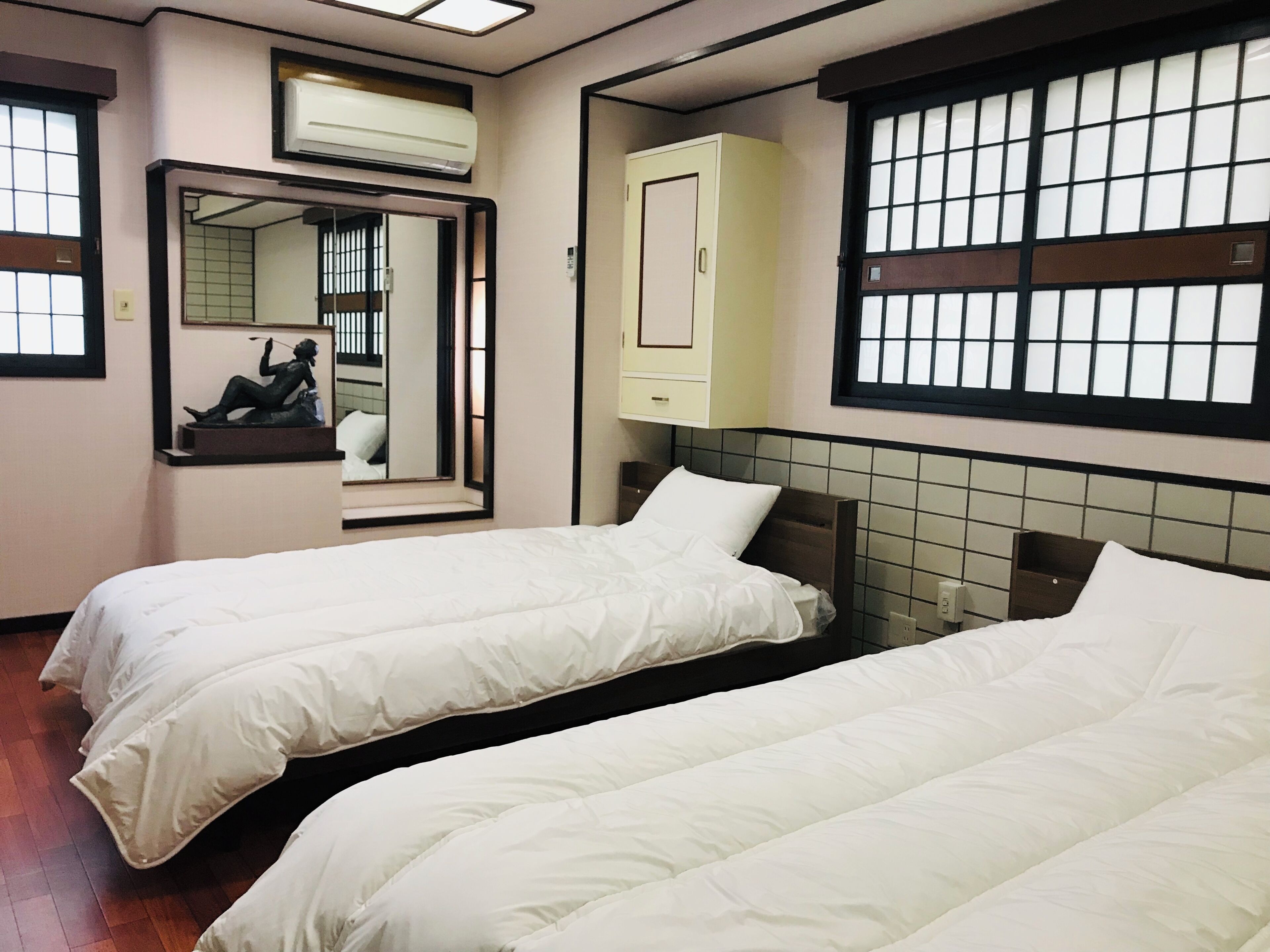 Een hotelkamer met twee bedden, een spiegel, een kledingkast en een raam met een rasterpatroon.