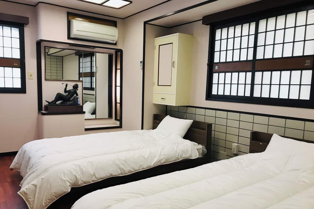 Een hotelkamer met twee bedden, een spiegel, een kledingkast en een raam met een rasterpatroon.