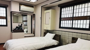 Ein Hotelzimmer mit zwei Betten, einem Spiegel, einem Kleiderschrank und einem Fenster mit Gittermuster.