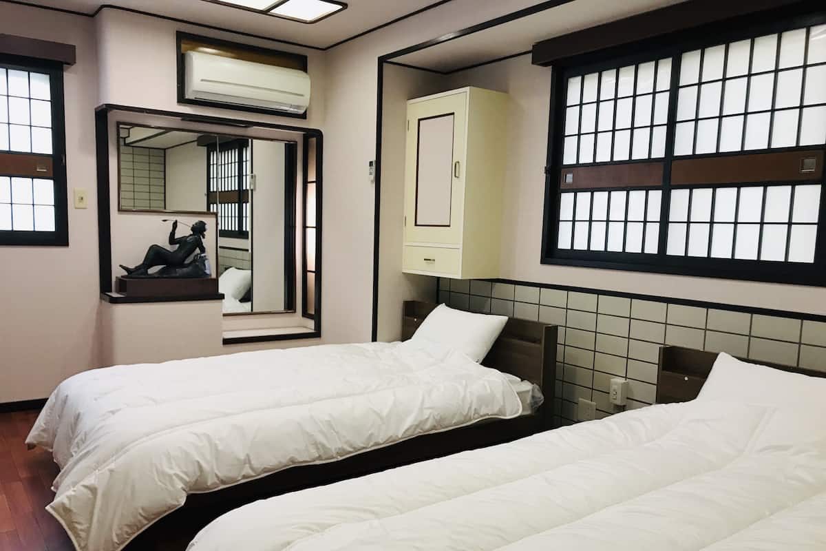 Een hotelkamer met twee bedden, een spiegel, een kledingkast en een raam met een rasterpatroon.
