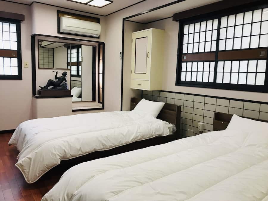 Habitación de hotel con dos camas, un espejo, un armario y una ventana con diseño de cuadrícula.