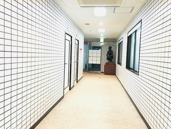 A corridor with tiled walls, a statue, and a door. - Guesthouse & Hotel RA Kagoshima (Kagoshima)