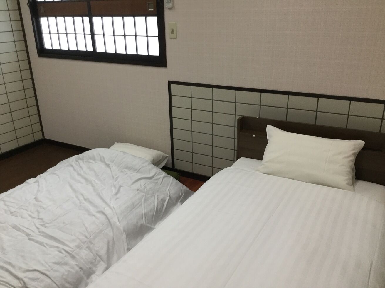 Ein Zimmer mit zwei Betten, einem vergitterten Fenster und einer gefliesten Wand.