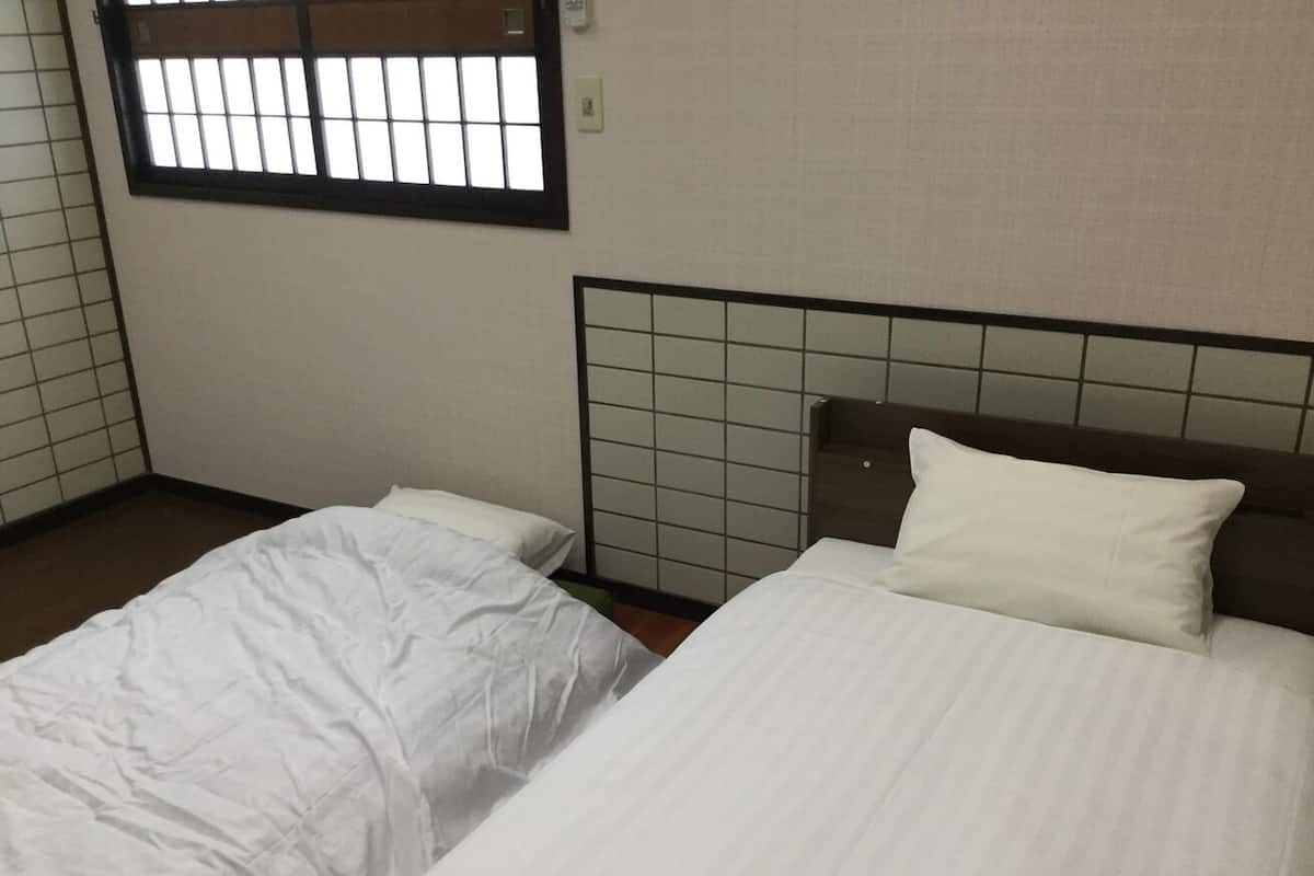 Een kamer met twee bedden, een raam met tralies en een betegelde muur.