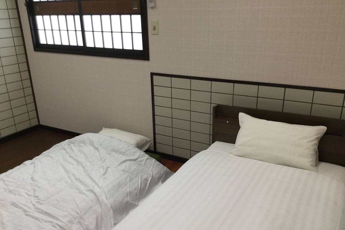 Een kamer met twee eenpersoonsbedden, een raam met tralies en een betegelde muur.