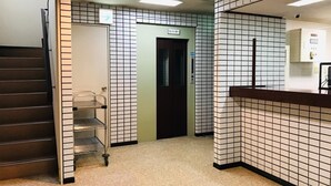 Un hall d’hôtel avec un sol carrelé, un comptoir d’accueil, un escalier et un ascenseur.