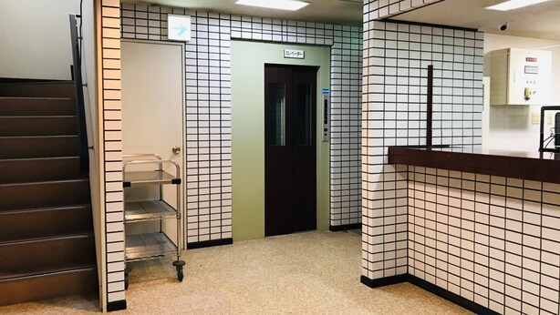 Eine Hotellobby mit Fliesenboden, einer Rezeption, einer Treppe und einem Aufzug.