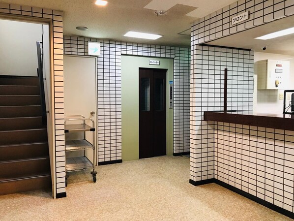 Um hall de hotel com piso de azulejos, balcão de recepção, escada e elevador.