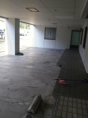 Uma área externa coberta com piso de azulejos, piso de concreto e uma mangueira verde à esquerda.