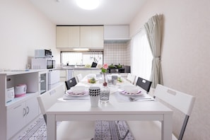 A modern kitchen with white cabinets, a dining table set for four, and a view of the adjacent living area.