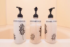 Trois flacons de produits pour les soins capillaires, dotés de pompes doseuses, étiquetés « Gel douche », « Shampooing » et « Soin capillaire », disposés sur une surface.