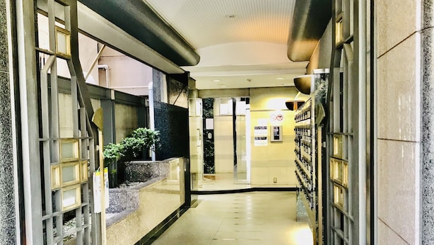 A corridor with a tiled floor, a glass door on the left, and a wall with a metal rack on the right. - Garden Otsuka 504 (Tokyo)