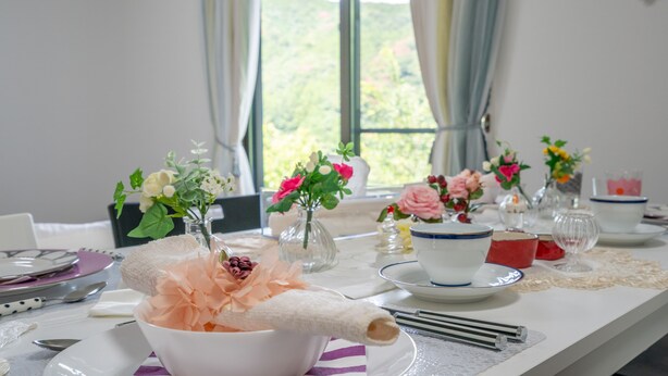 Ett matbord dukat med vita och blå tallrikar, skålar och bestick, dekorerat med rosa och vita blommor i glasvaser.