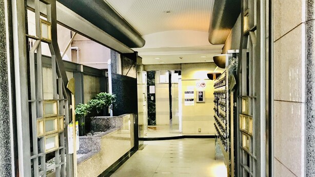 A corridor with a tiled floor, a glass door on the left, and a wall with a metal rack on the right. - Garden Otsuka 704 (Tokyo)