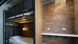 A compact room with a bunk bed, wooden flooring, a brick wall, and a hanging light fixture. - Connector Hostel (Makati)
