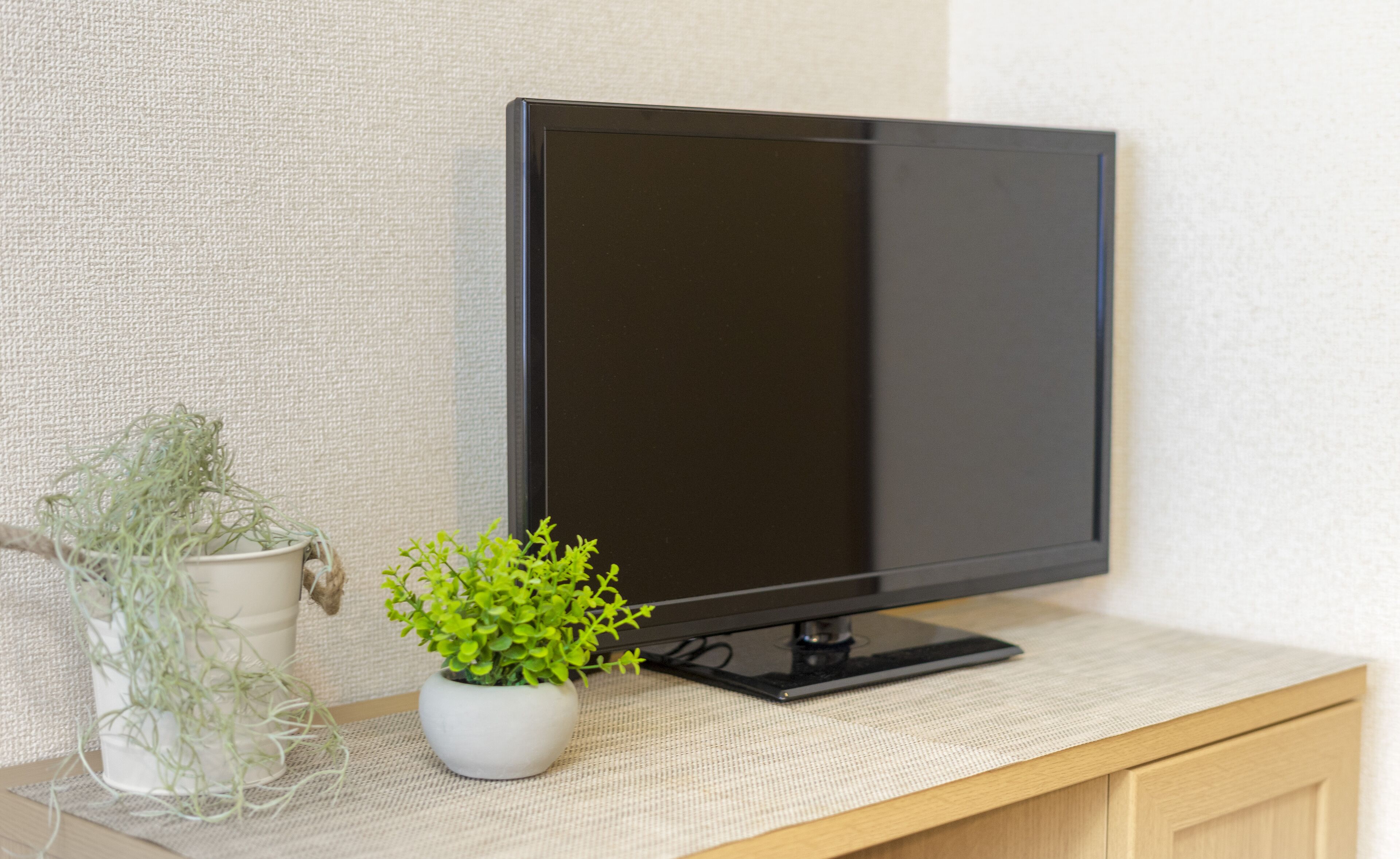 A flat-screen TV on a wooden desk with a white pot and green plant beside it.