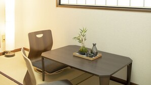 Een traditionele Japanse kamer met tatami vloerbedekking, een lage tafel met een vaas en een plant, en twee stoelen.