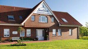 Une maison à deux étages en briques, avec une enseigne indiquant « Seeblick Ferienwohnungen » et un numéro de téléphone.