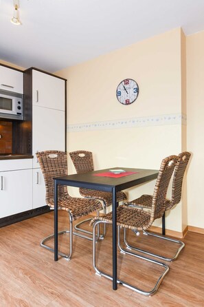 A dining area with a table and four wicker chairs, a clock on the wall, and a microwave in the background.