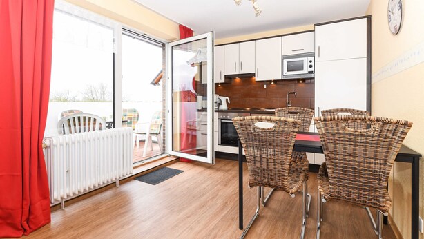 Une cuisine moderne avec des meubles blancs, un four à micro-ondes et une cuisinière. On y trouve des chaises et une table en osier dans l’espace repas.