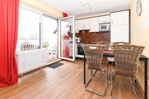 A modern kitchen with white cabinets, a microwave, and a stove. There are wicker chairs and a table in the dining area.
