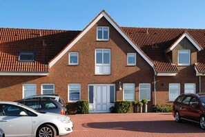 A two-story brick house with a red-tiled roof, a white door, and multiple windows. There are two cars parked in the driveway.