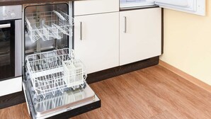 Une cuisine compacte équipée d’un lave-vaisselle encastré, d’un four à micro-ondes et d’un réfrigérateur dont la porte est ouverte.