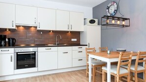 Une cuisine moderne avec des meubles blancs, un four encastré et un coin repas comprenant une table et des chaises en bois.
