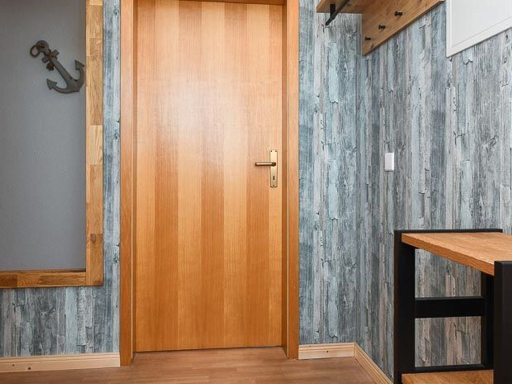 A wooden door with a brass handle, a small table with a black frame, and a rustic wall with a distressed wood finish.