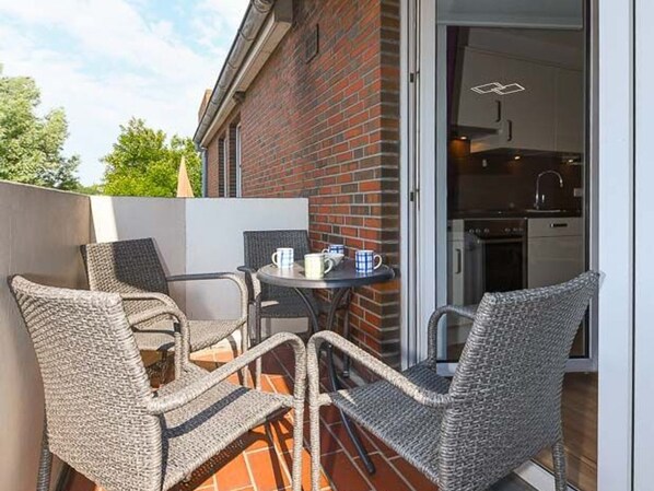 An outdoor patio area with wicker chairs and a table, a brick wall, and a sliding glass door leading to a kitchen. - Vacation beach shell (Wittmund)