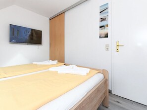 A hotel room with a bed, a television mounted on the wall, and a door with a golden handle. - Apartment North Sea view (Wittmund)