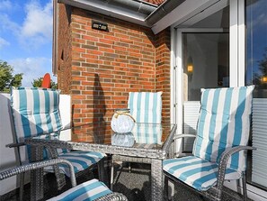 A patio with wicker furniture and striped cushions, a glass table, and a brick wall. - Apartment North Sea view (Wittmund)