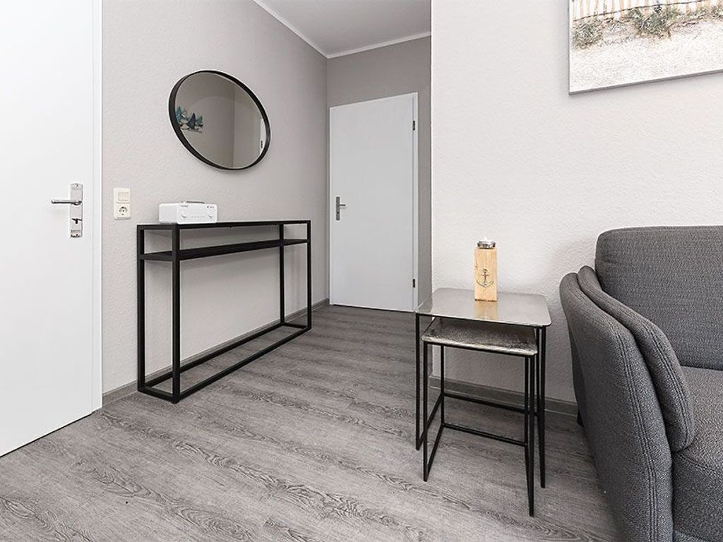A modern room with a grey sofa, a small table with a lamp, a black console table, and a round mirror on the wall.