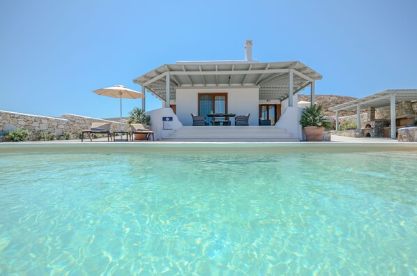 A poolside area with a covered seating area, stone walls, and a clear view of the pool.
