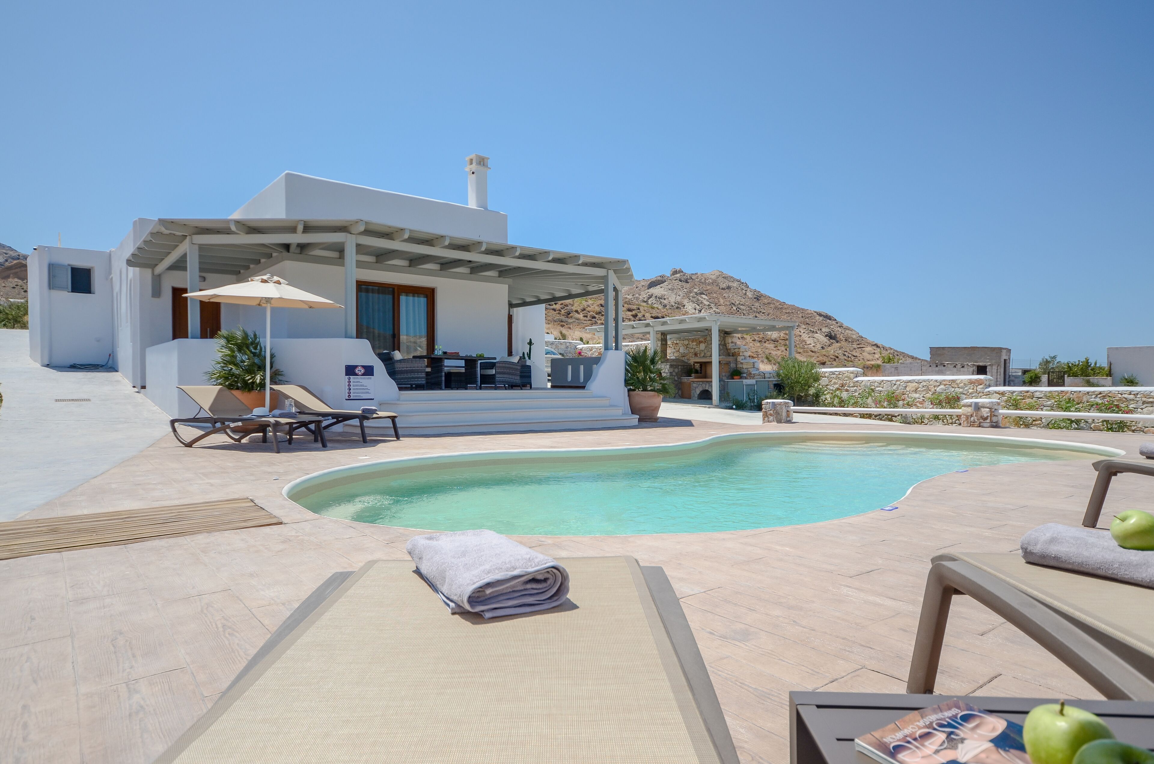 A modern outdoor pool area with lounge chairs, a covered seating area, and a mountain view.