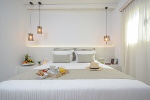A neatly made bed with a breakfast tray, pillows, and a hat on the bedside table.