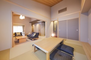 Uma sala de estar moderna com uma mesa de jantar de madeira, sofá e uma pequena mesa de centro. Há uma porta deslizante que dá para outro cômodo.