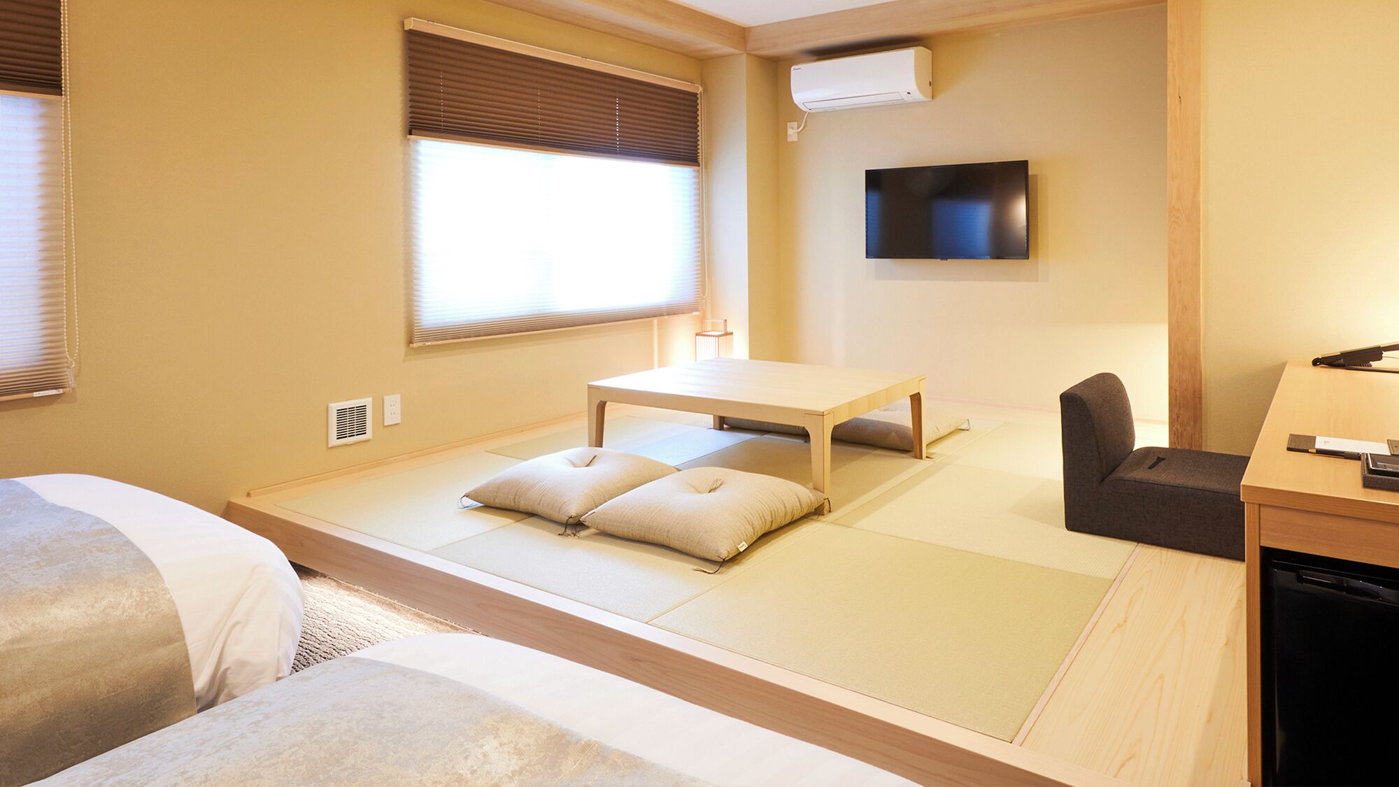 A traditional Japanese room with tatami flooring, a low table, a sofa, a TV, and a heater.