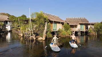 Two people paddleboarding on a calm river with traditional houses on the banks.