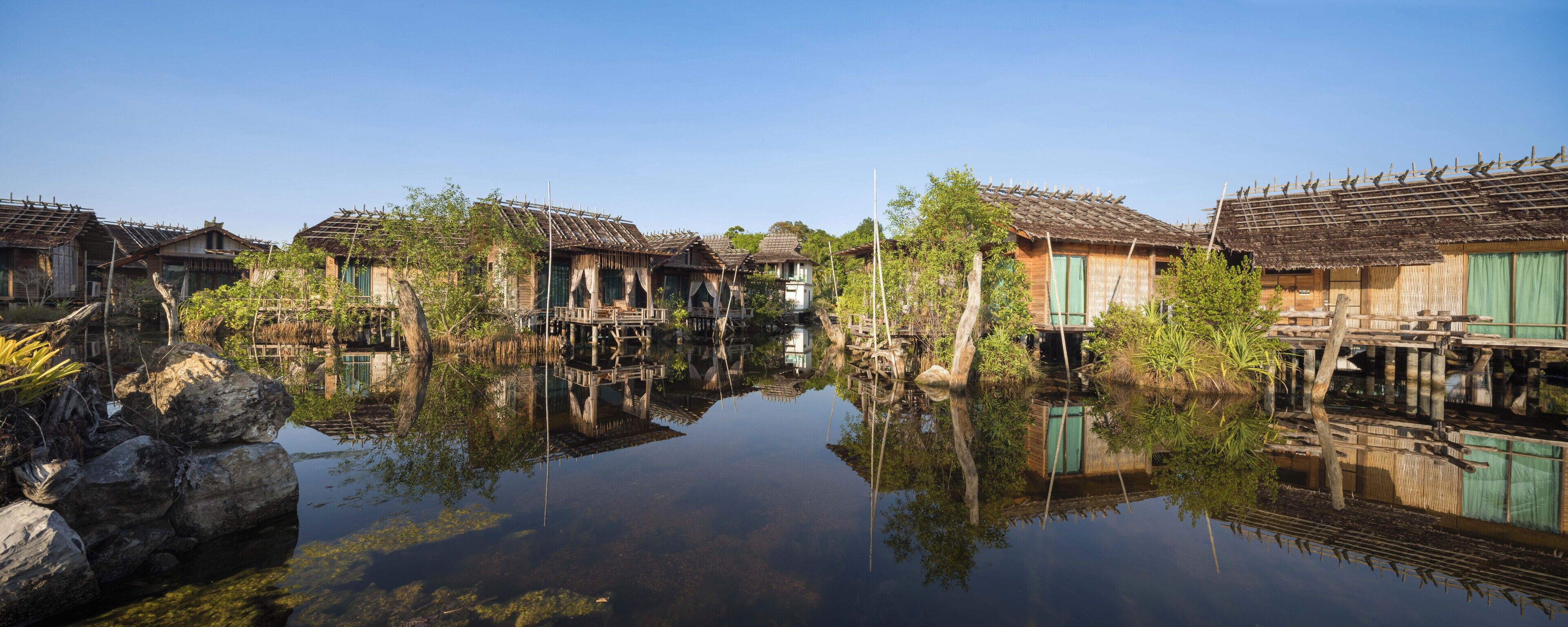 Une maison traditionnelle en bois, avec un toit de chaume, située au bord d’un plan d’eau paisible.