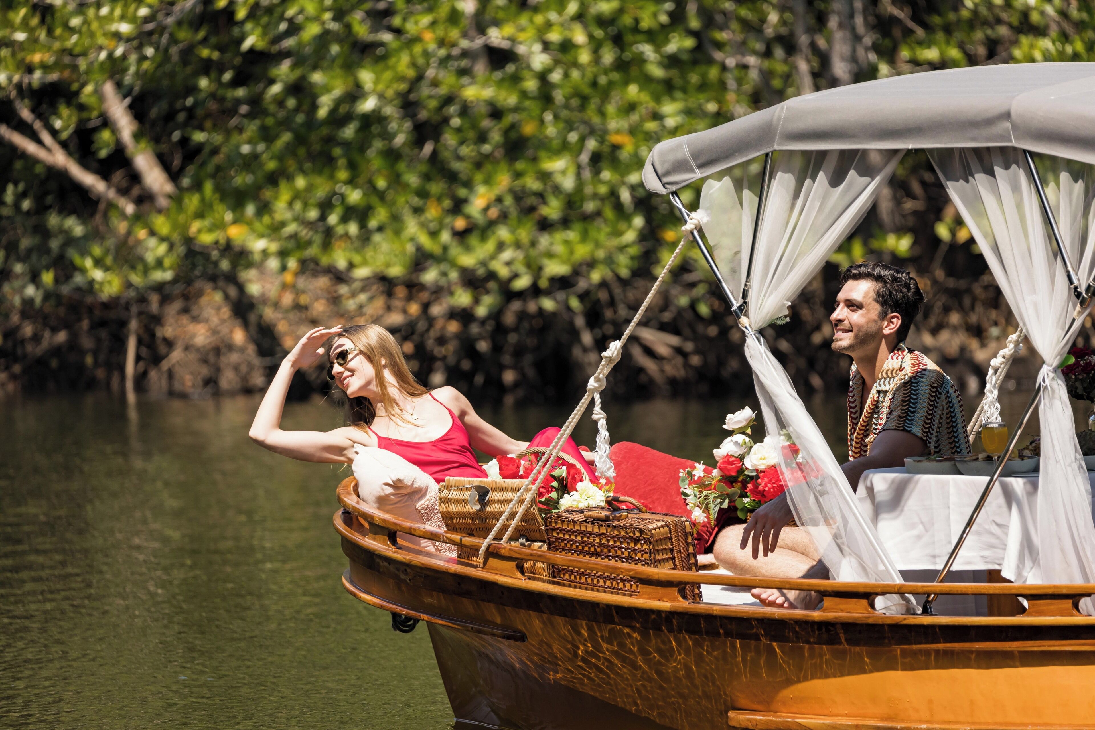 A boat with a canopy and wicker furniture, surrounded by water and greenery.