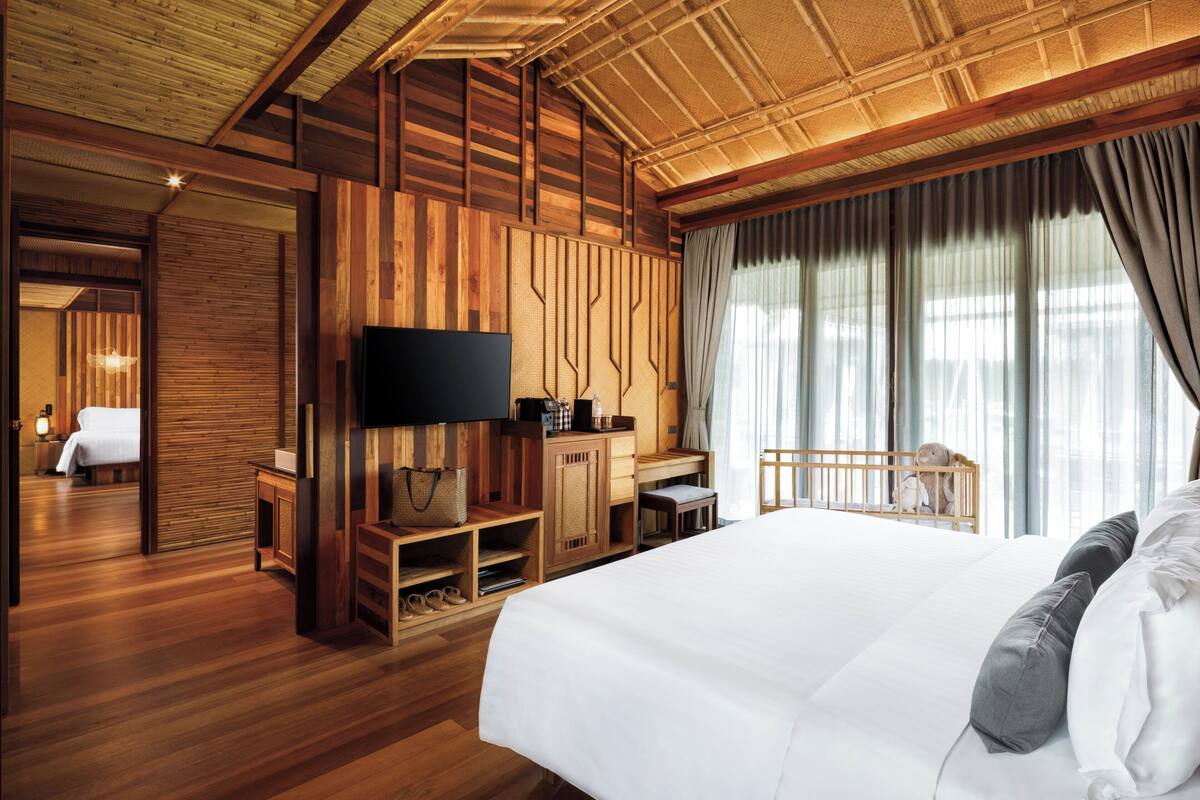 A wooden-themed hotel room with a bed, TV, desk, and a view of the outdoors.