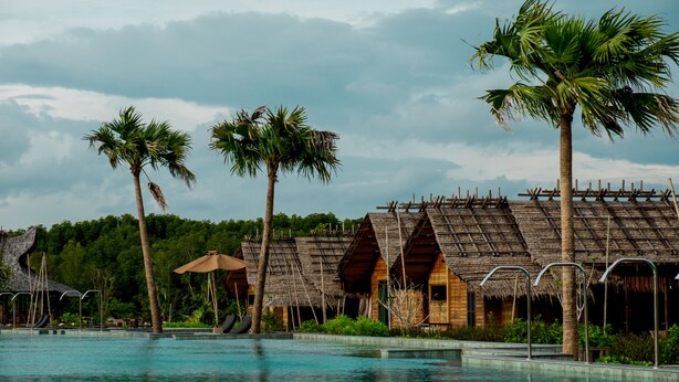 A resort with a swimming pool, thatched-roof huts, palm trees, and a forested backdrop. - Venice Krabi Villa Resort (Krabi)