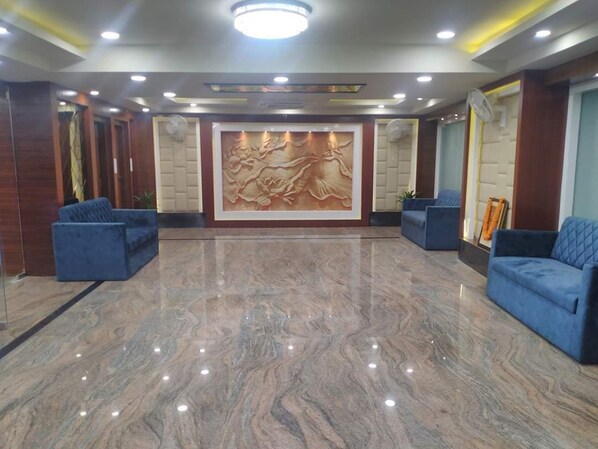 A lobby with marble flooring, blue sofas, and a large wall mural. - Hotel SJR (Varanasi)