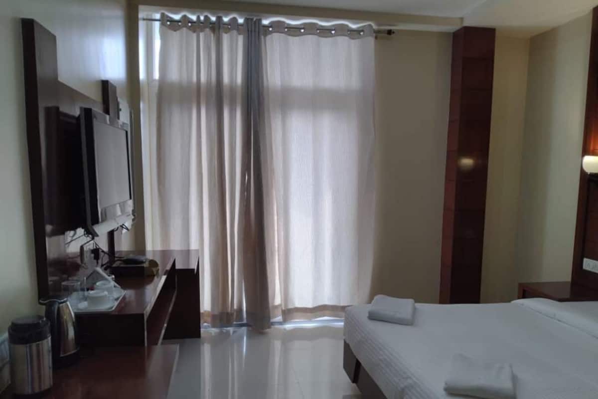 A hotel room with a bed, a desk with a computer, a TV, and a window with curtains.