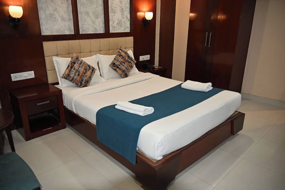 A hotel room with a large bed, a nightstand, a wardrobe, and wall sconces.
